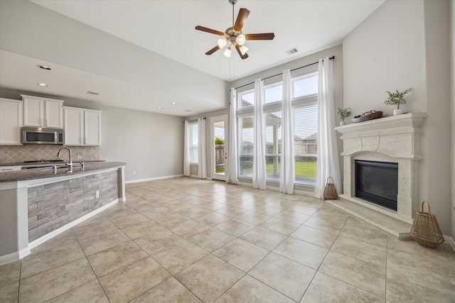 unfurnished living room featuring visible vents, light tile patterned flooring, a fireplace, baseboards, and a ceiling fan