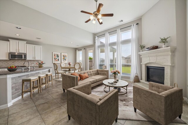living room with visible vents, a glass covered fireplace, baseboards, a ceiling fan, and light tile patterned floors