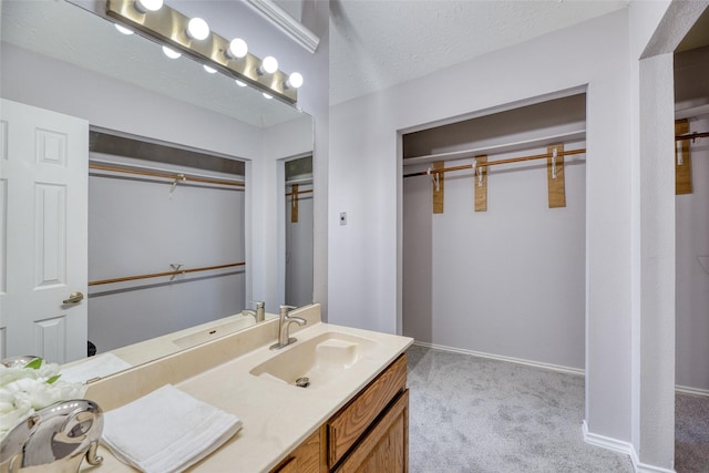bathroom with baseboards, a textured ceiling, a walk in closet, and vanity