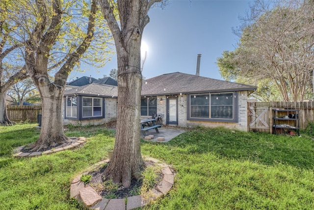 rear view of house with a lawn, brick siding, fence, a patio, and a shingled roof