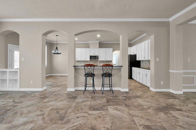 kitchen with crown molding, stainless steel microwave, dark countertops, and a kitchen bar