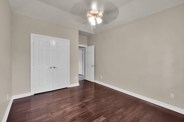 unfurnished bedroom with a closet, baseboards, ceiling fan, and dark wood-type flooring