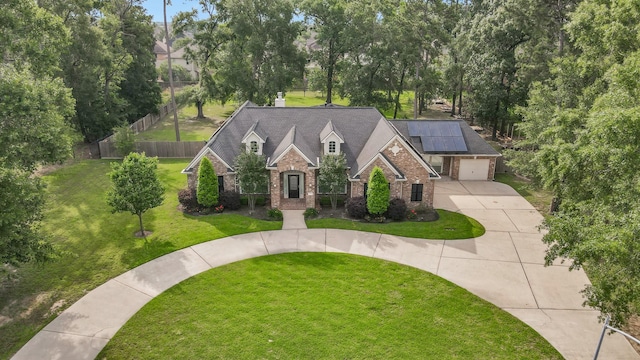 view of front of property featuring driveway, a front yard, brick siding, fence, and roof mounted solar panels