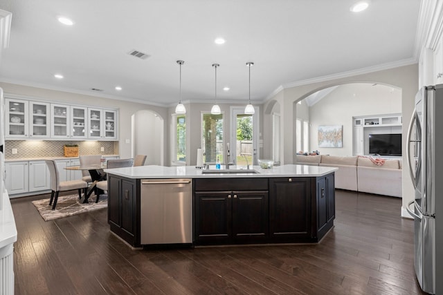 kitchen featuring appliances with stainless steel finishes, a sink, light countertops, arched walkways, and a center island with sink