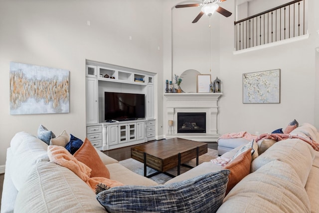 living room with a glass covered fireplace, ceiling fan, and a high ceiling