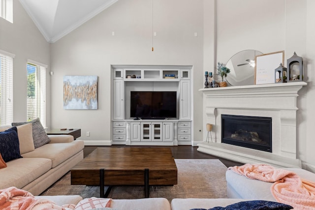 living area featuring high vaulted ceiling, baseboards, dark wood-style floors, a glass covered fireplace, and ornamental molding