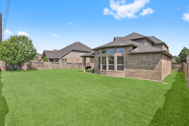 rear view of property featuring a lawn, brick siding, a fenced backyard, and roof with shingles