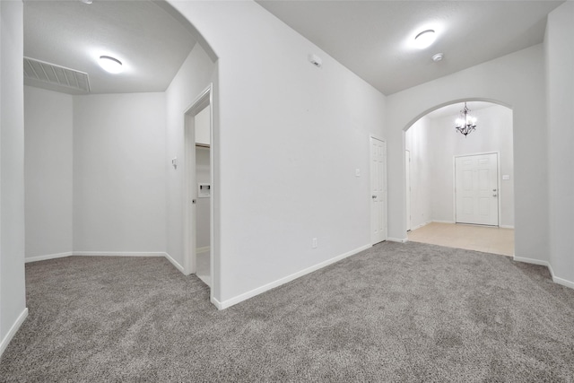 carpeted spare room featuring arched walkways, baseboards, a notable chandelier, and visible vents
