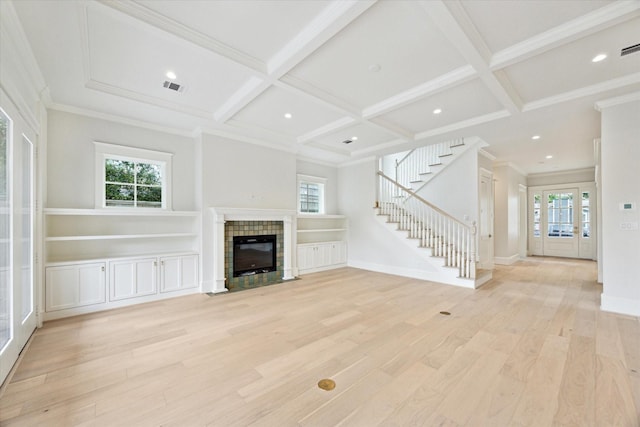 unfurnished living room featuring light wood-style flooring, stairs, a tile fireplace, plenty of natural light, and coffered ceiling