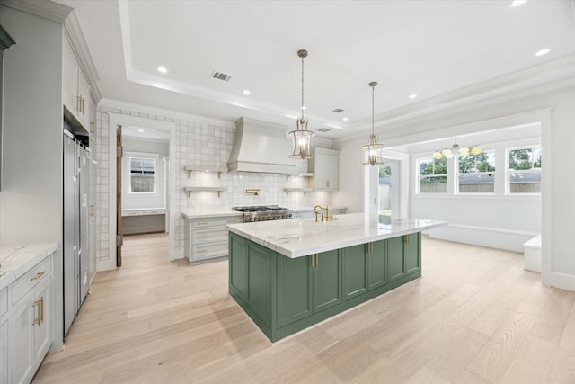 kitchen featuring green cabinets, custom exhaust hood, light wood-type flooring, a raised ceiling, and crown molding