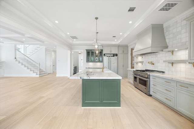 kitchen with high quality appliances, custom exhaust hood, backsplash, light wood finished floors, and crown molding