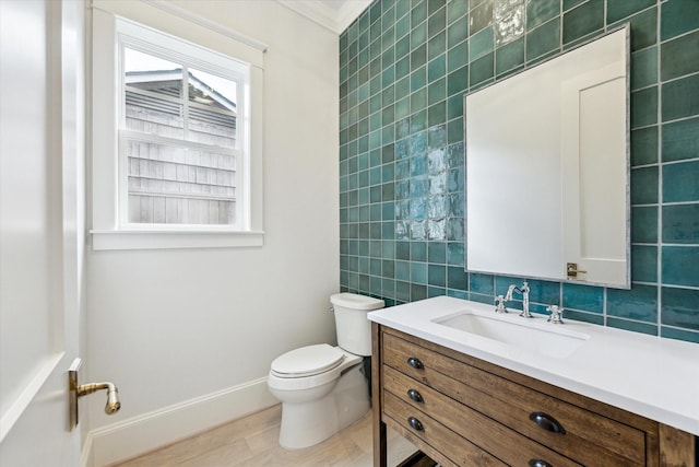 half bathroom featuring tile walls, toilet, crown molding, vanity, and baseboards