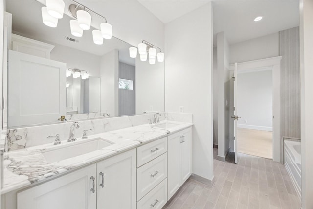 full bath with double vanity, wood finished floors, a bathtub, and baseboards