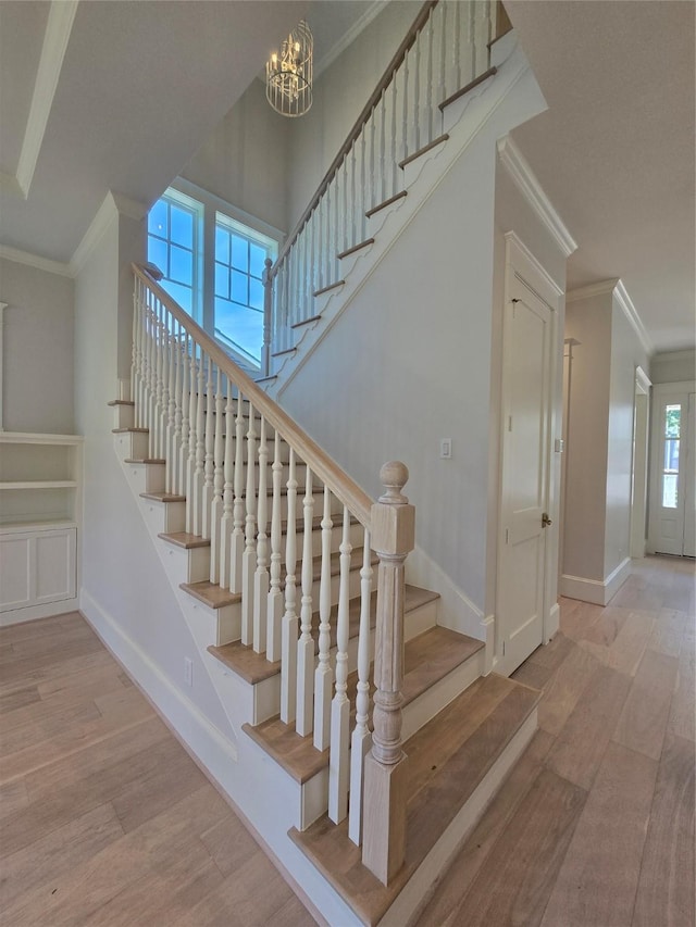 stairway with crown molding, wood finished floors, baseboards, and a chandelier