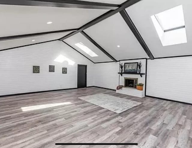 additional living space featuring a skylight, a fireplace with raised hearth, wood finished floors, and brick wall