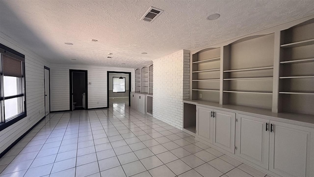 empty room with healthy amount of natural light, a textured ceiling, built in features, light tile patterned floors, and brick wall