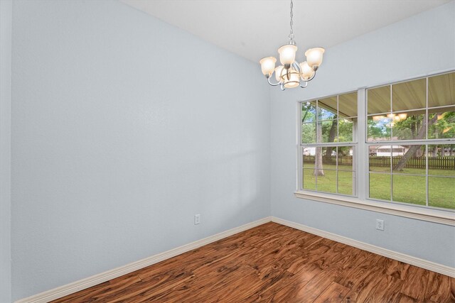 empty room featuring an inviting chandelier, baseboards, and wood finished floors