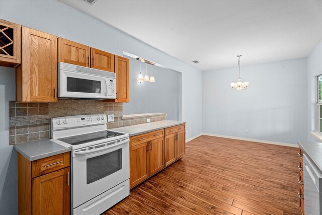 kitchen with decorative backsplash, wood finished floors, white appliances, a chandelier, and hanging light fixtures