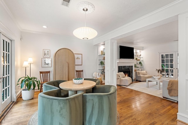 dining space featuring light wood-style floors, ornamental molding, a fireplace, and visible vents