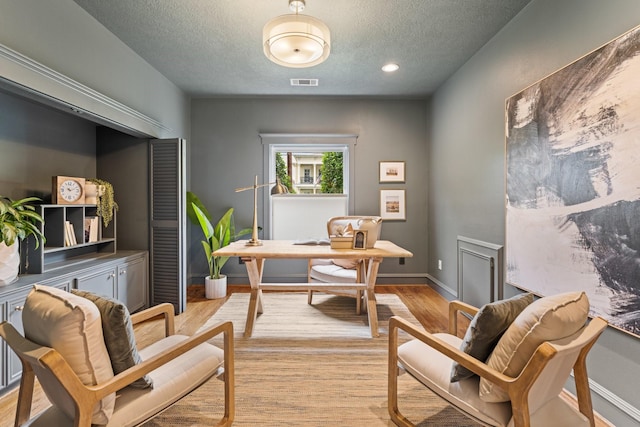 office featuring a textured ceiling, visible vents, baseboards, and light wood-style floors