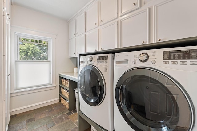 laundry room featuring cabinet space, baseboards, washer and clothes dryer, and stone tile flooring