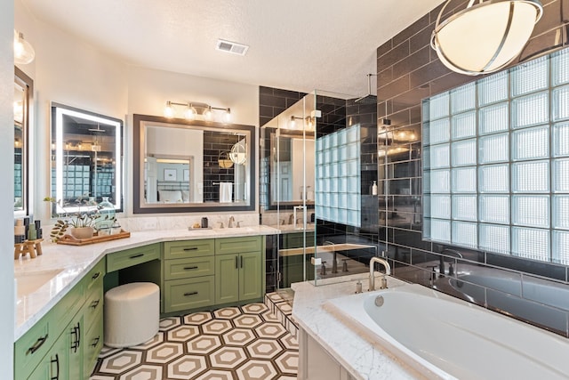 bathroom featuring visible vents, vanity, a textured ceiling, a bath, and a tile shower