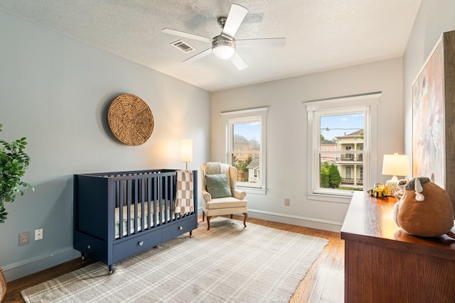 bedroom featuring ceiling fan, a crib, light wood-style flooring, baseboards, and visible vents