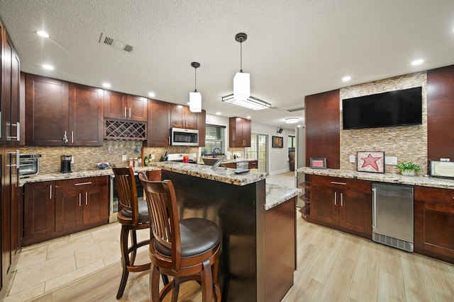 kitchen featuring a breakfast bar, stainless steel microwave, decorative backsplash, light wood-type flooring, and visible vents
