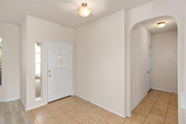 entrance foyer featuring light tile patterned floors, arched walkways, and baseboards