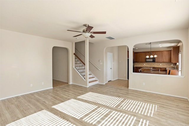 unfurnished living room with light wood-style floors, arched walkways, ceiling fan with notable chandelier, stairs, and visible vents