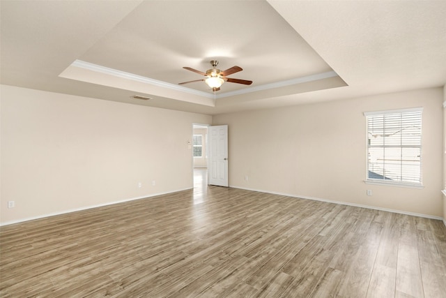 spare room featuring crown molding, ceiling fan, light wood-style flooring, baseboards, and a tray ceiling