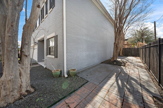 view of property exterior featuring brick siding, a fenced backyard, and a patio