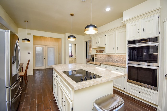 kitchen with decorative backsplash, wood finish floors, a center island, appliances with stainless steel finishes, and decorative light fixtures