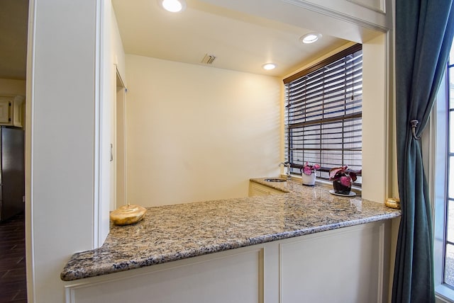 kitchen featuring light stone countertops, a sink, freestanding refrigerator, white cabinetry, and visible vents
