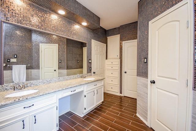 full bath featuring a sink, tiled shower, wood finish floors, and double vanity
