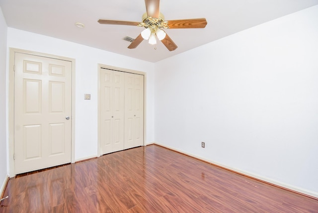 unfurnished bedroom with visible vents, a closet, wood finished floors, baseboards, and a ceiling fan