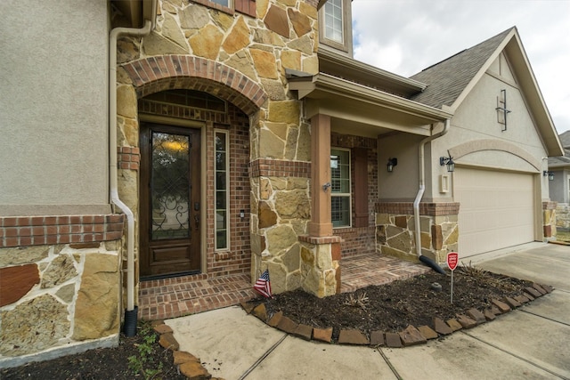 view of exterior entry with stone siding, stucco siding, brick siding, a shingled roof, and concrete driveway