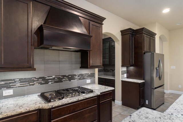 kitchen with appliances with stainless steel finishes, dark brown cabinetry, custom exhaust hood, and arched walkways