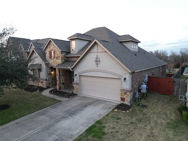 view of front facade with a shingled roof, a front lawn, driveway, and stone siding