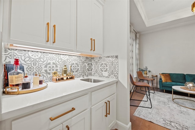 bar featuring a sink, decorative backsplash, ornamental molding, and wood finished floors