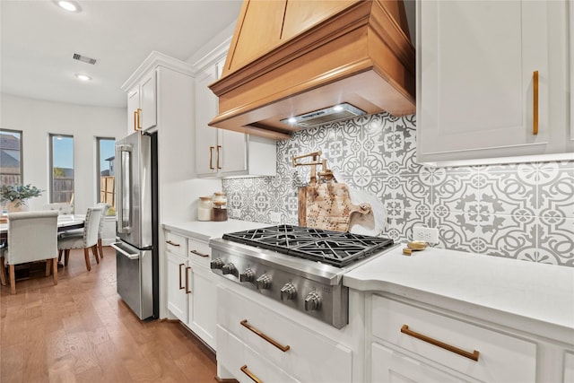 kitchen with visible vents, wood finished floors, white cabinets, custom range hood, and appliances with stainless steel finishes