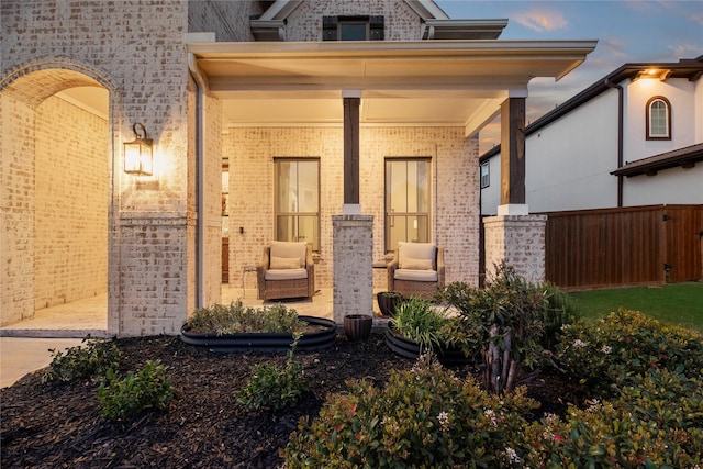 view of exterior entry featuring a porch, fence, and brick siding