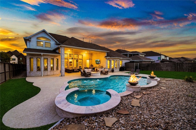 rear view of house featuring a pool with connected hot tub, brick siding, an outdoor living space with a fire pit, a fenced backyard, and a patio area