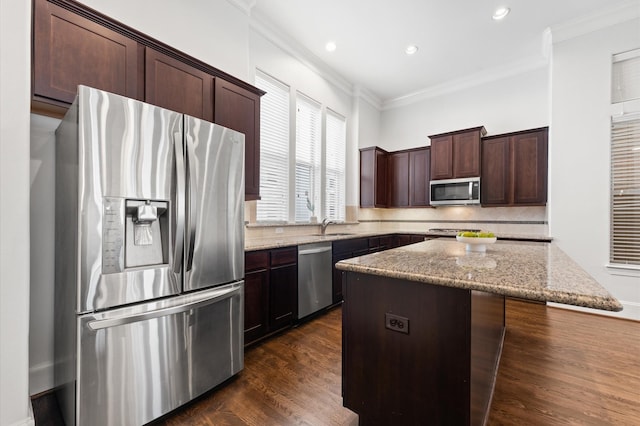 kitchen featuring backsplash, crown molding, a center island, light stone counters, and stainless steel appliances