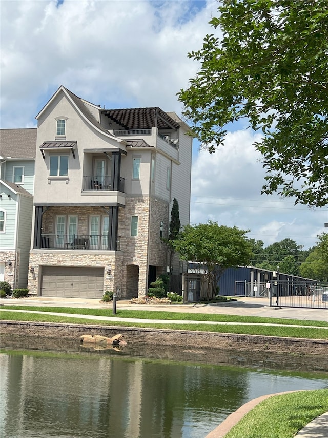 exterior space with a balcony, a water view, an attached garage, stone siding, and stucco siding