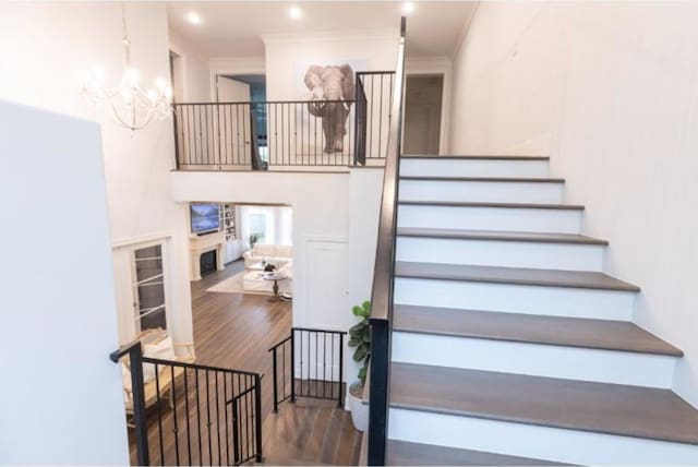 stairs featuring ornamental molding, a fireplace, wood finished floors, and a notable chandelier
