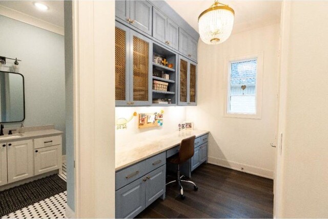office with dark wood finished floors, built in desk, a sink, baseboards, and a notable chandelier