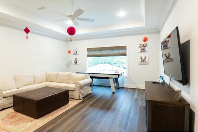 living area with ceiling fan, crown molding, wood finished floors, a raised ceiling, and baseboards
