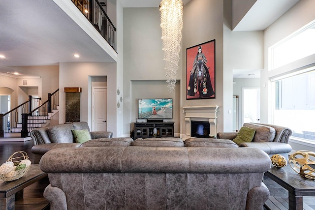 living room with a high ceiling, arched walkways, a glass covered fireplace, stairs, and recessed lighting