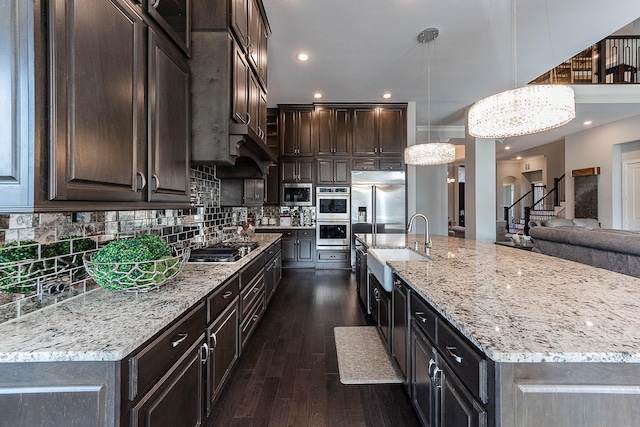 kitchen featuring dark brown cabinets, an inviting chandelier, light stone counters, built in appliances, and dark wood-style floors